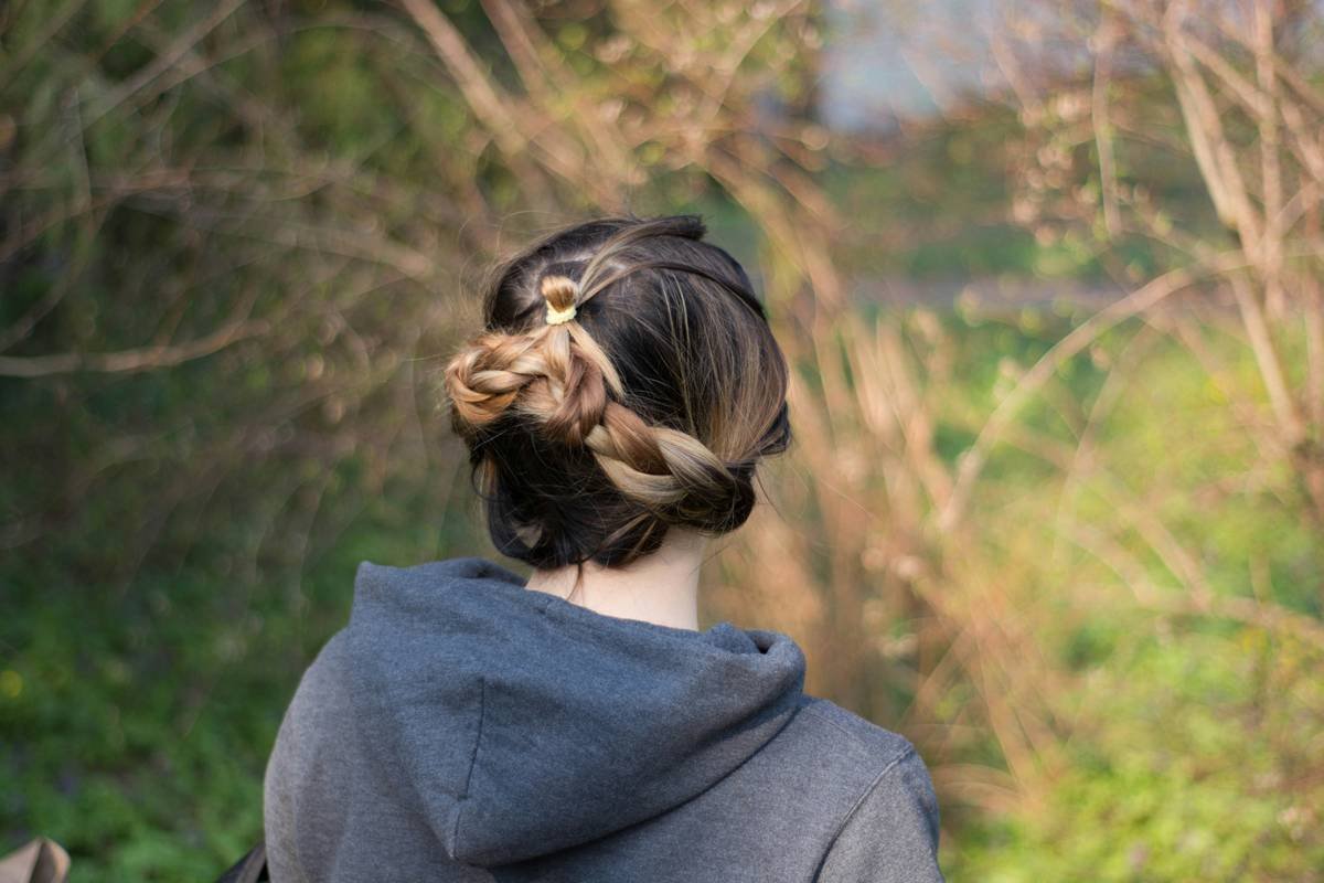 A runner holding messy hair after jogging with sweat dripping down her face.