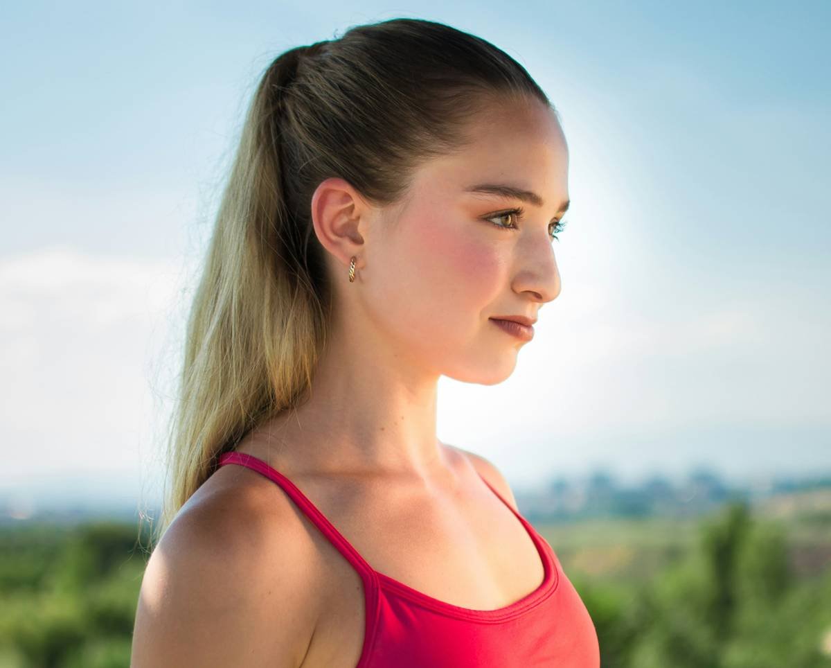 Infographic showing traction alopecia risk zones on scalp during common gym hairstyles: high ponytail, tight bun, braided crown. Red zones highlight temple and hairline areas under strain.