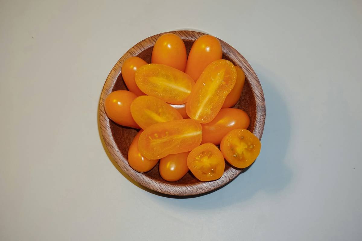 Sun-Kissed Sweetness: Golden Delights of Yellow-Dattelwein Cherry Tomatoes by Raju C Reddy Embrace the radiance of summer's finest through this exquisite top-view still-life photograph by the accomplished Raju C Reddy. Set within a rustic wooden bowl, a captivating cluster of Yellow-Dattelwein cherry tomatoes takes center stage, their golden hues glowing like drops of sunshine captured in nature's bounty. As if to offer a taste of their succulent sweetness, three tomatoes have been meticulously sliced and arranged atop the bunch.